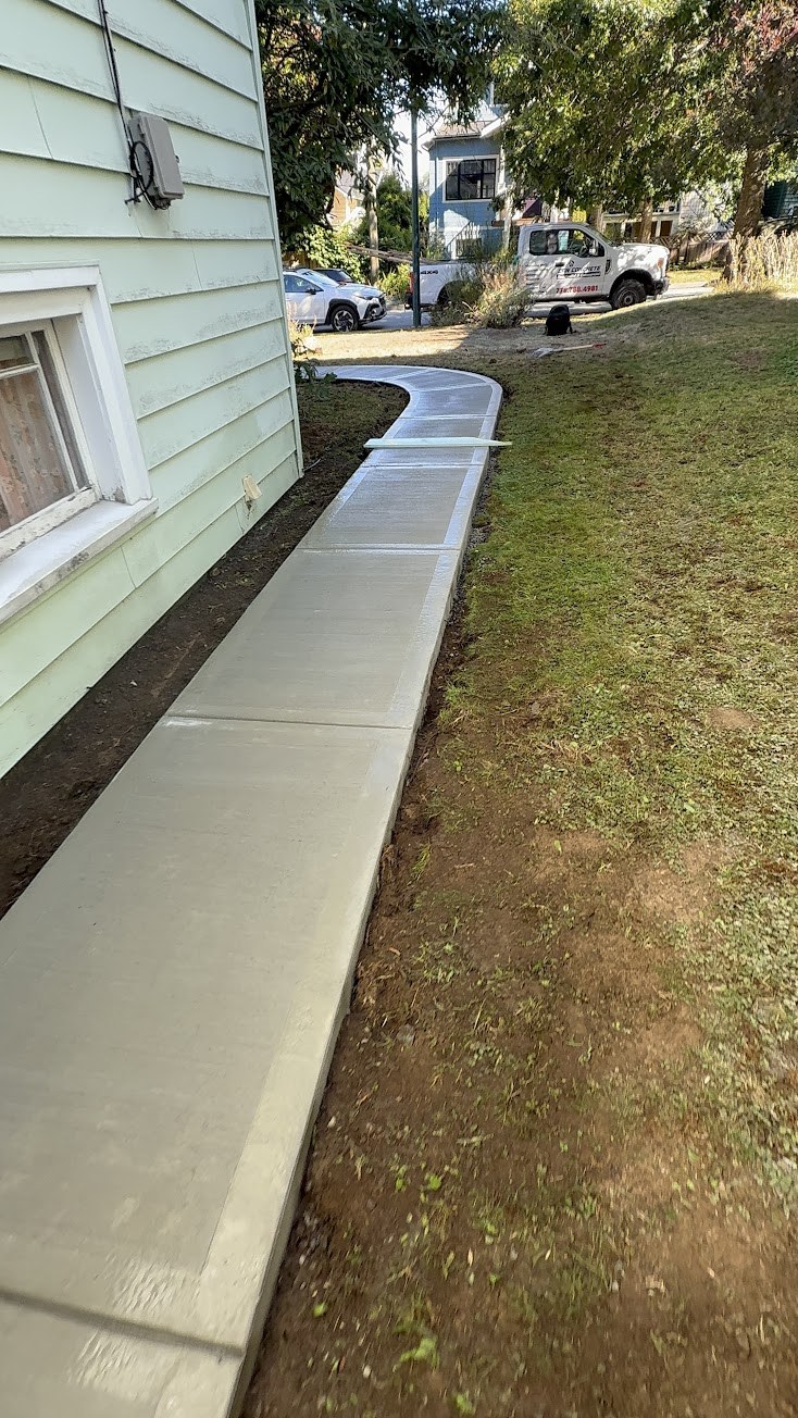 Finished curved concrete walkway along a house in South Vancouver with a white work truck parked on the street
