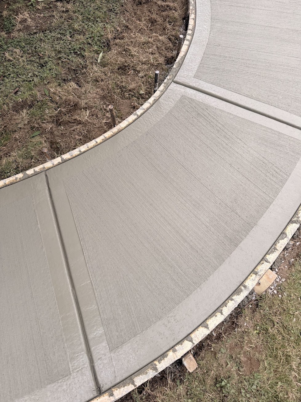 Close-up of a curved concrete walkway showing a broom-finish centre with smooth trowelled border bands in South Vancouver