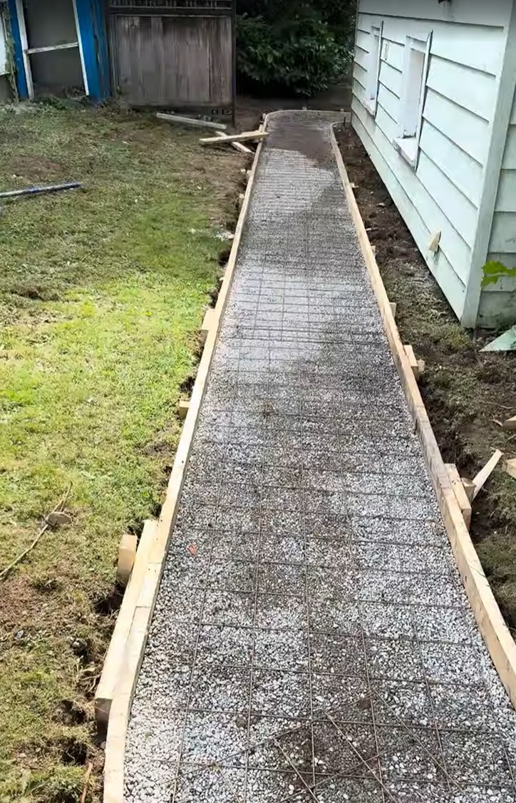 Compacted gravel base with wire mesh laid in before pouring a curved concrete walkway in South Vancouver