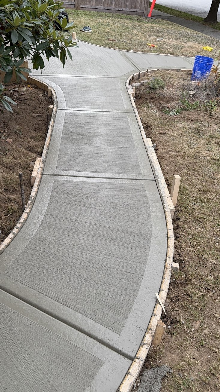 Freshly finished curved concrete walkway with smooth border bands and broom-finish centres, wooden forms still in place in South Vancouver