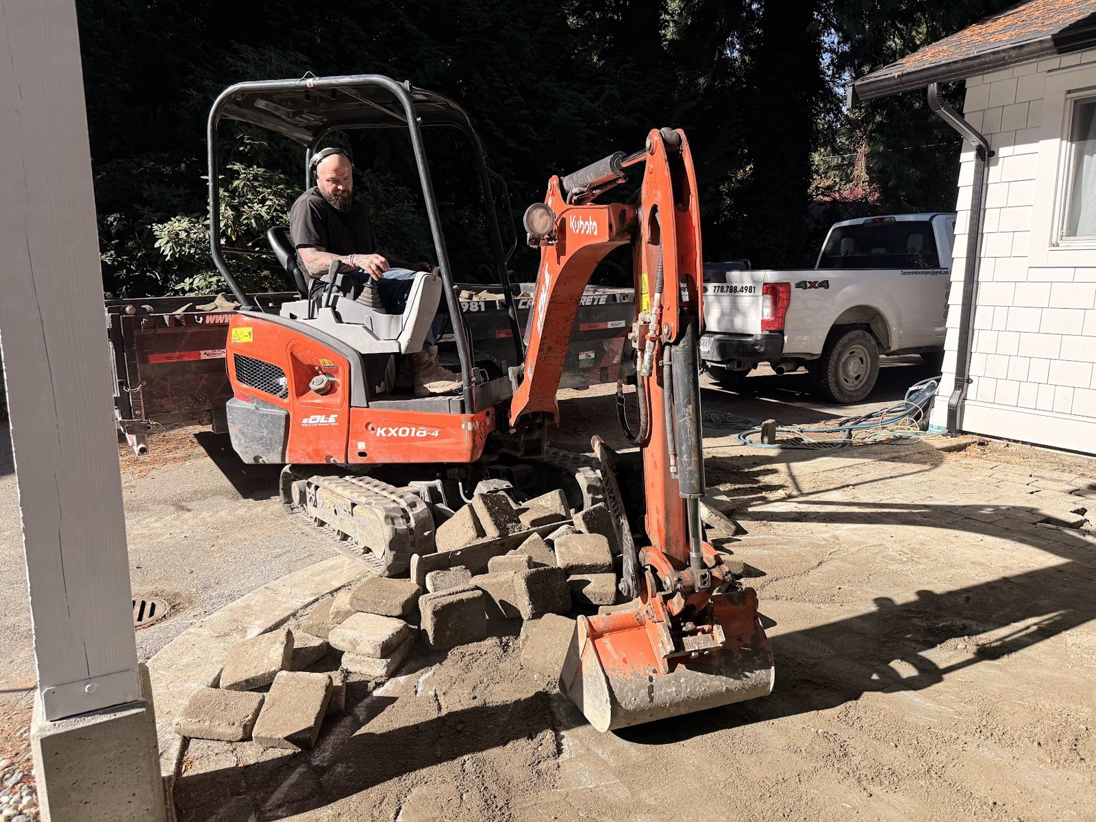 Mini excavator removing old pavers from a backyard patio in Surrey BC