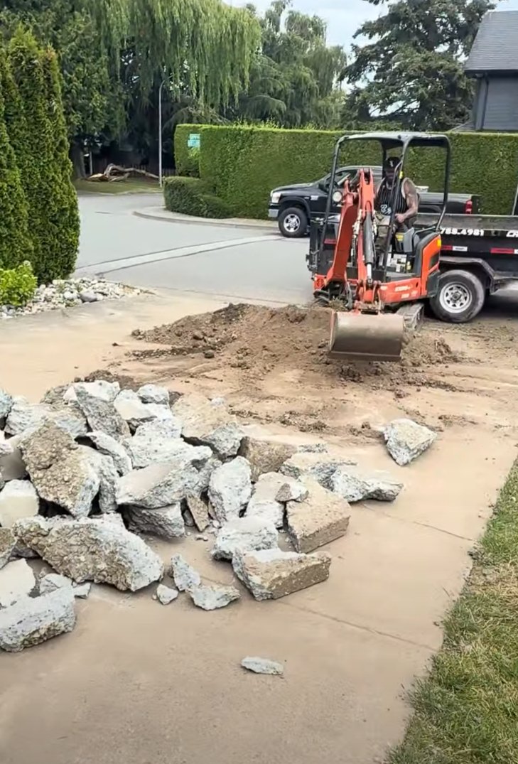 Mini excavator breaking out an old concrete driveway during removal in Steveston, Richmond BC