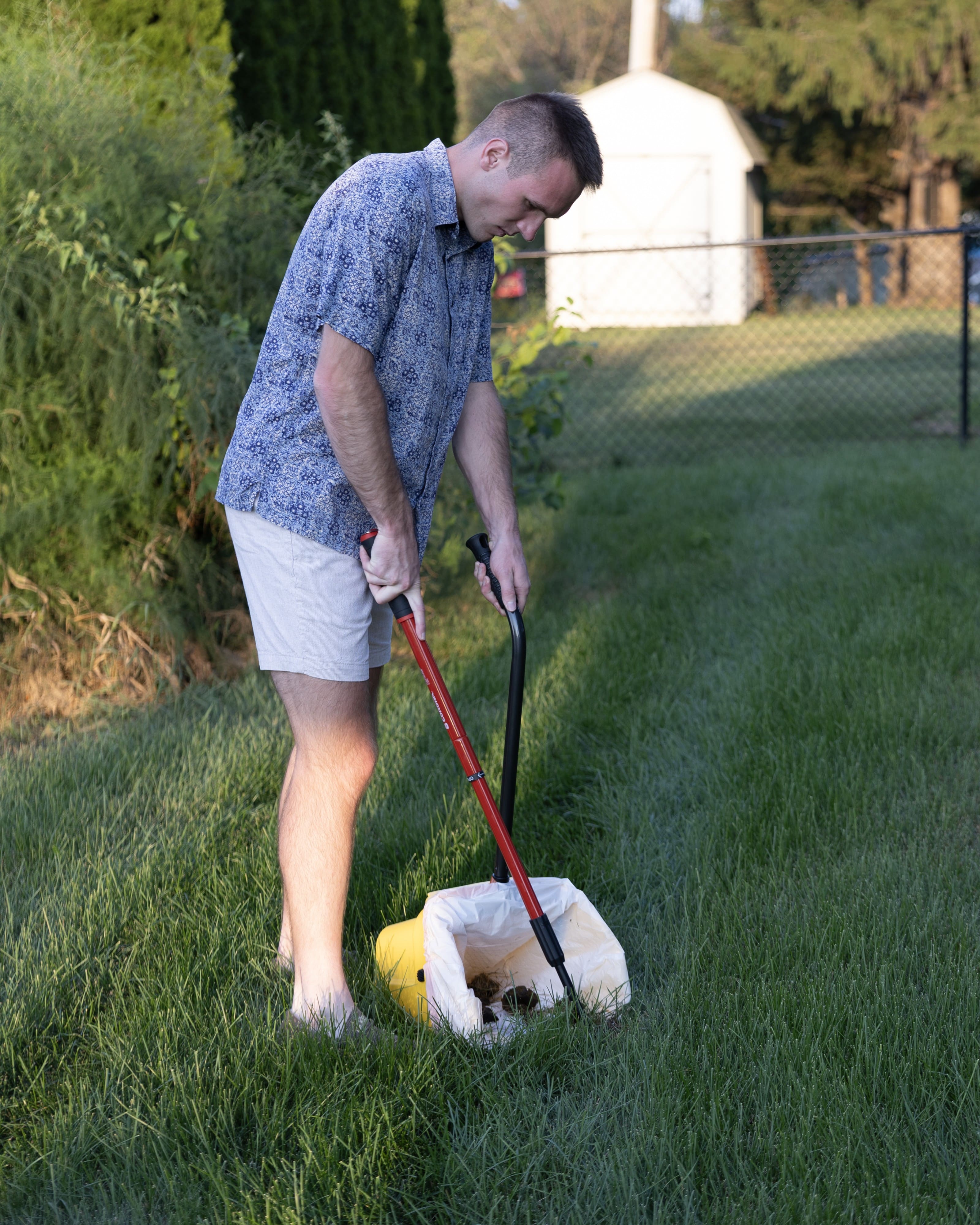 Logan from Number Two Crew performing residential dog waste cleanup with scooping equipment in a backyard