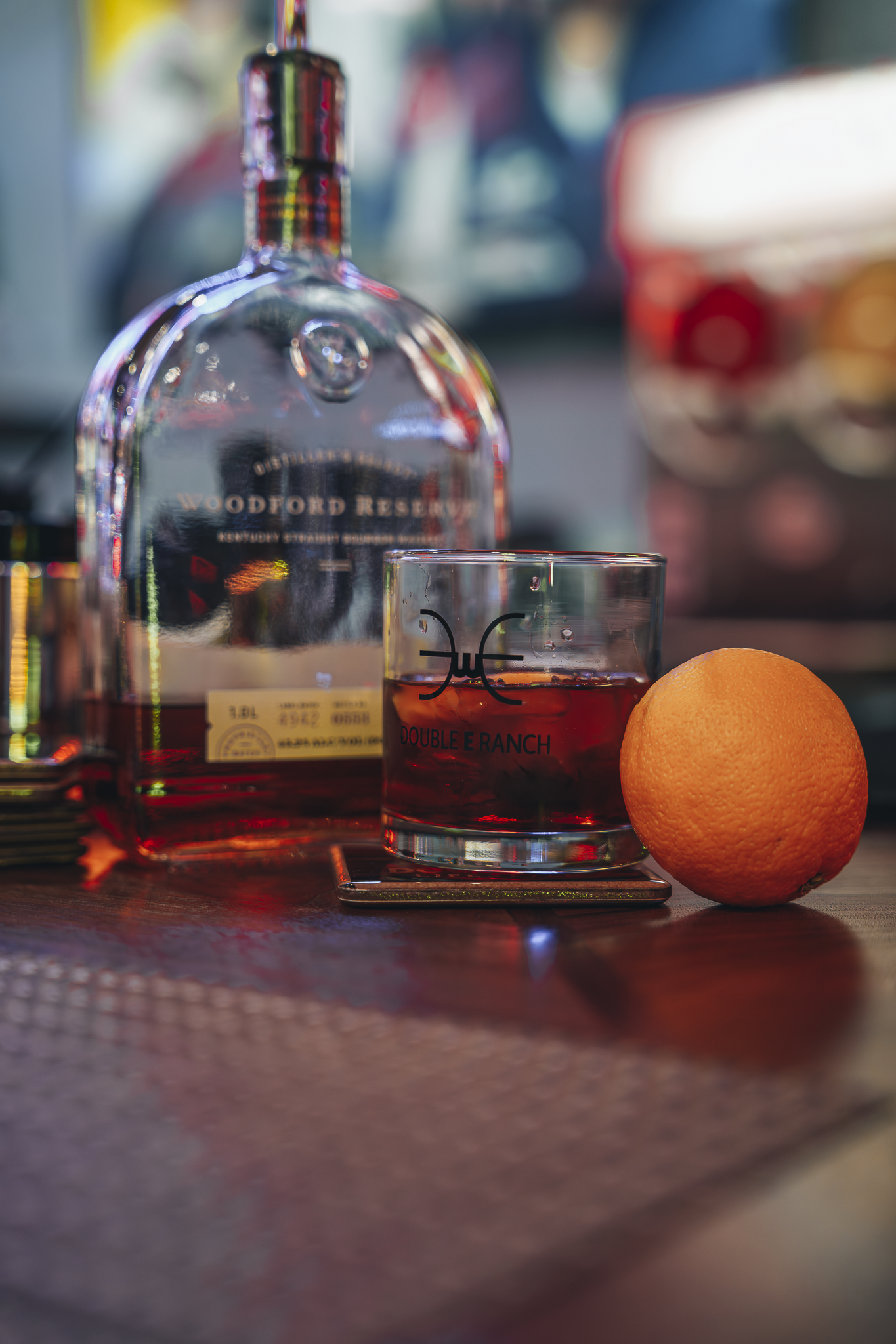 Double E Lifestyle bar setup with bourbon, orange slice, and branded rocks glass.