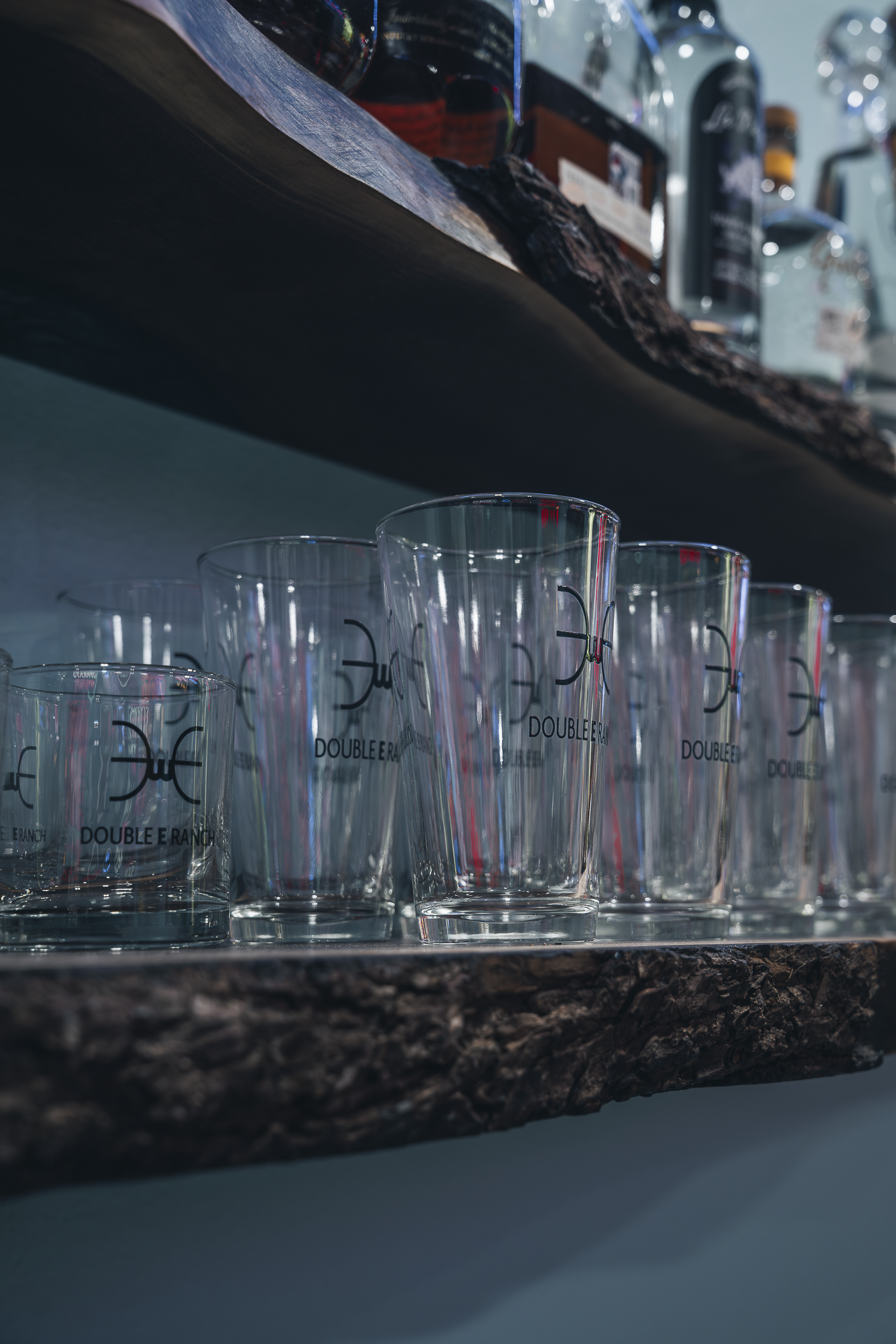 Double E Lifestyle branded glassware on a rustic wooden shelf, showcasing experiences and events in