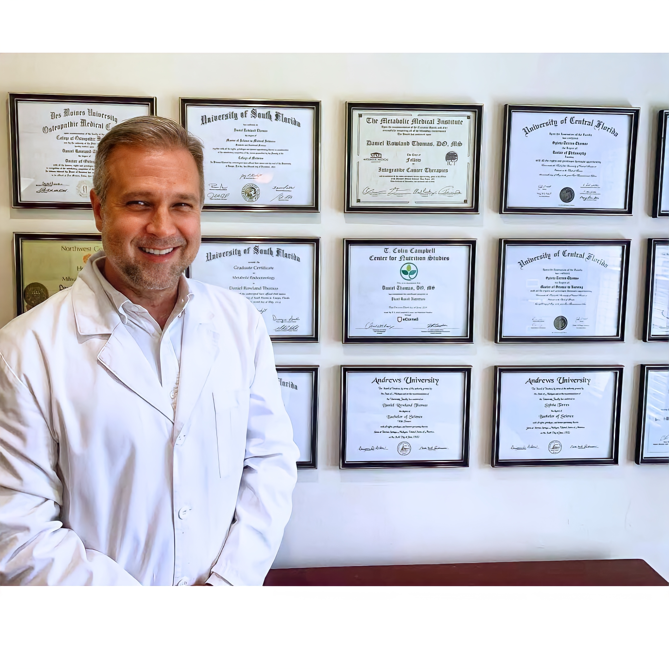 Dr. Daniel Thomas standing in front of his medical diplomas and certifications