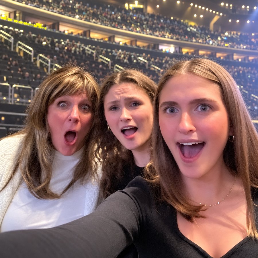 Mary and her two daughters taking a surprised selfie at an arena