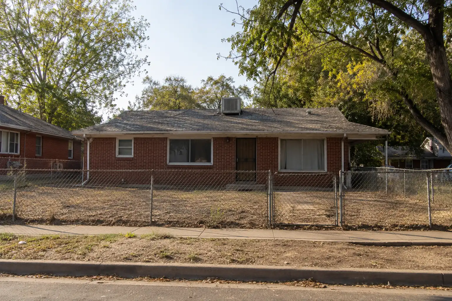 Worn brick ranch house in Denver with a dry lawn and chain-link fence
