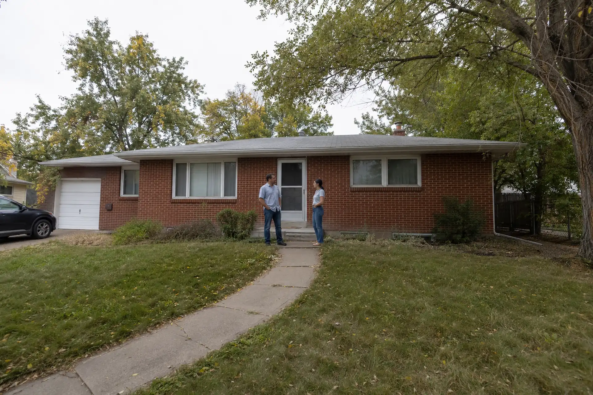 Two team members standing in front of a 1950s brick ranch house in Denver