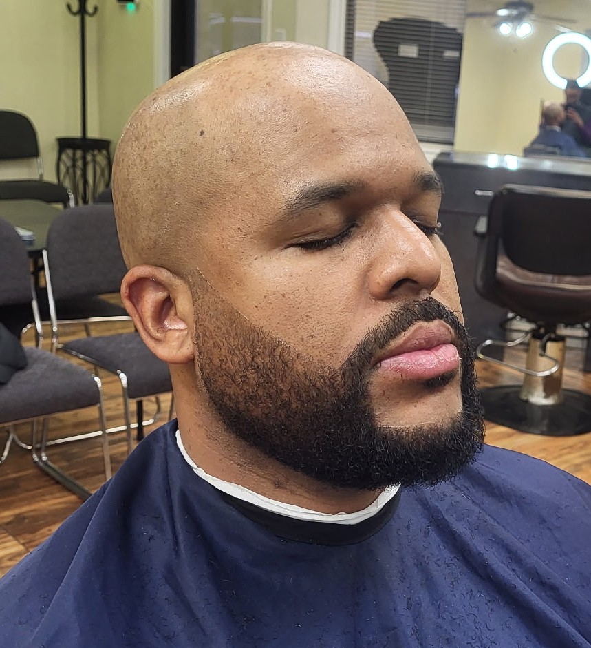 Clean-shaven head with a full, sharply lined beard
