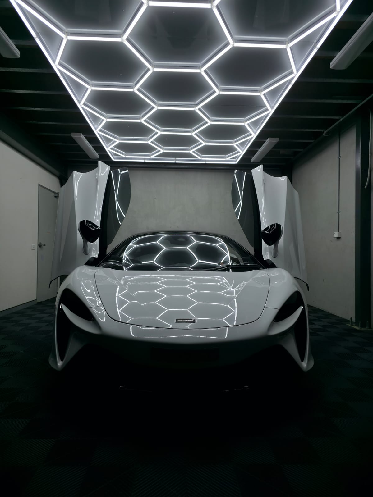 White McLaren with doors open in dimly lit detailing studio
