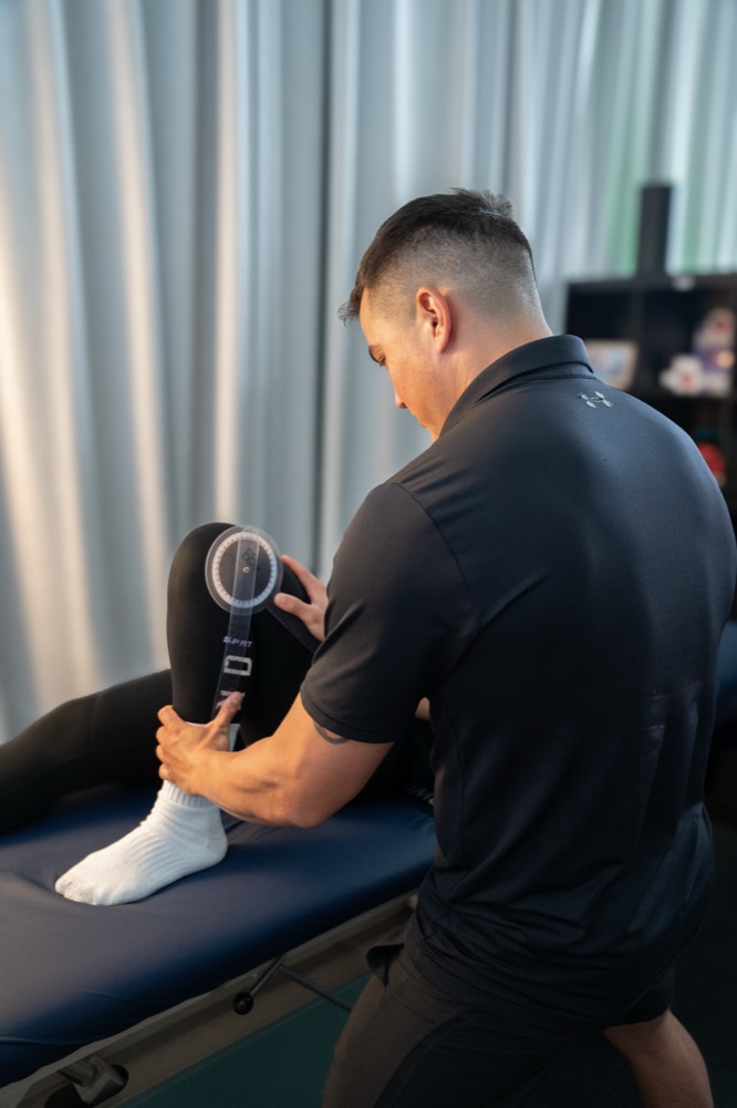Physiotherapist using a percussion massage gun on a client's leg