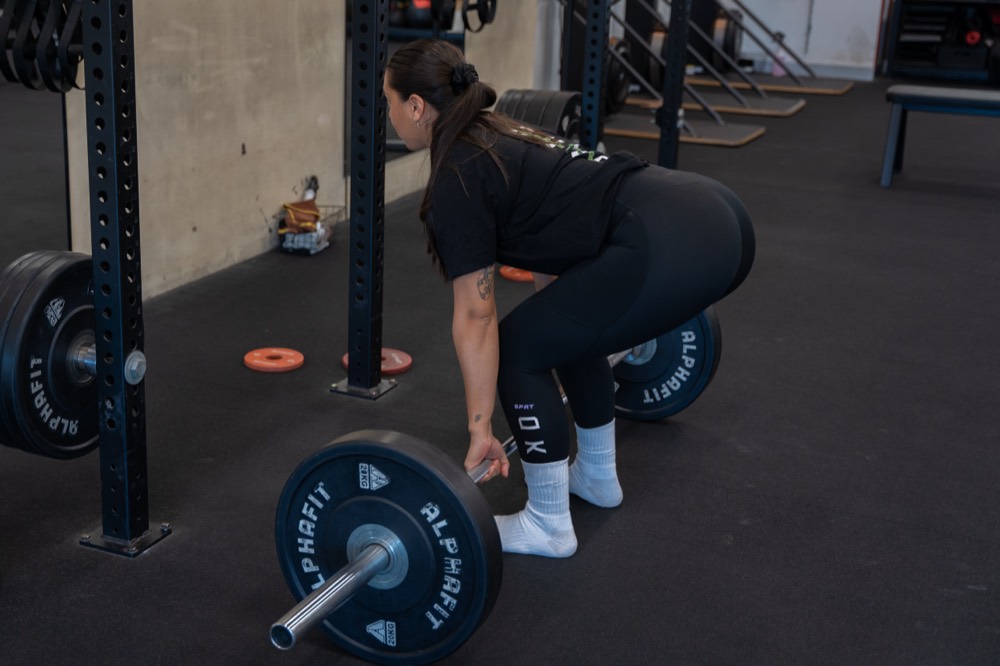 Client performing a barbell deadlift as part of strength-based rehab