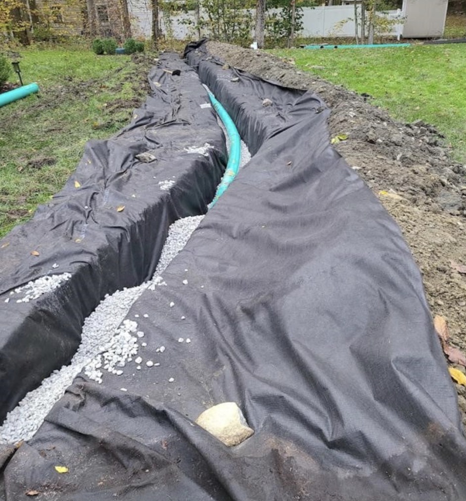 French drain trench with perforated pipe and gravel installed to redirect groundwater