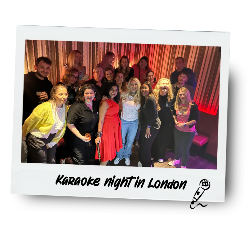 A group of people smiling and posing for a photo in a karaoke bar in London, with a colourful striped wall in the background. The photo has a white border with the text 'Karaoke night in London' and a small microphone icon.