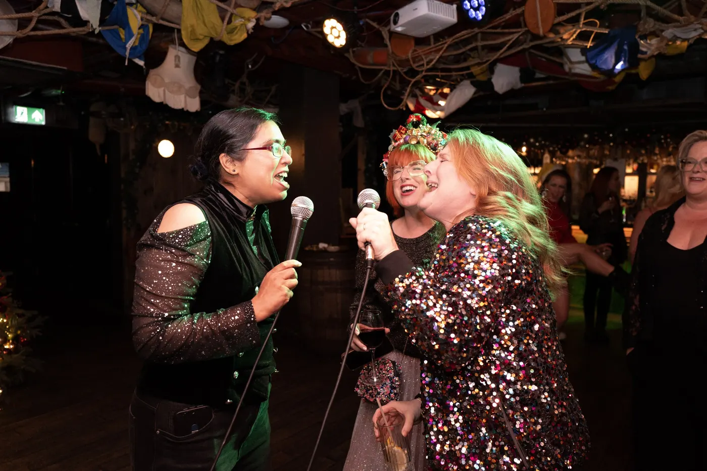 Two members belting out karaoke in sparkly outfits