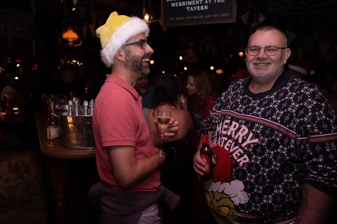 Members in festive hats and a Merry Whatever jumper at the bar