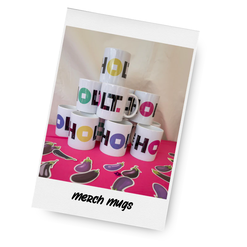 A collection of white ceramic mugs with colourful printed text, stacked in a pyramid shape on a pink surface, with eggplant stickers in front and the text 'merch mugs' at the bottom.