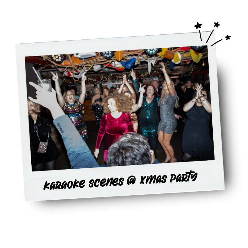 People dancing and singing at a Christmas party with festive decorations and colourful lighting, captured in a photo frame with the caption "Karaoke scenes @ Xmas party."