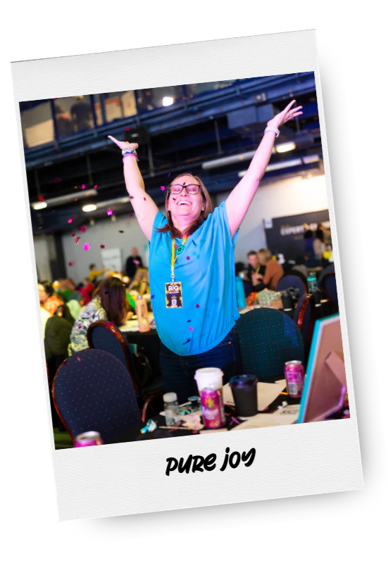 A woman celebrating with her arms raised and smiling at an indoor event, with confetti falling around her.