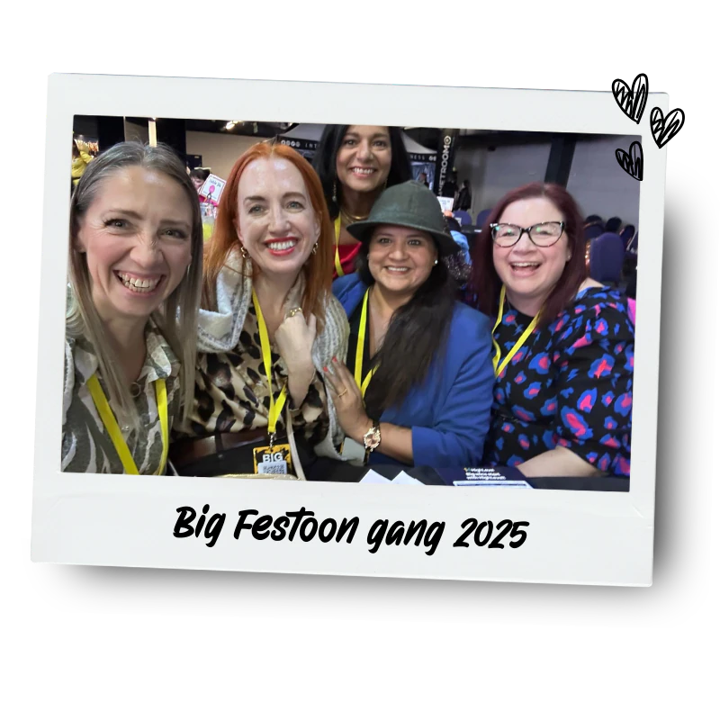 Five women smiling and posing for a photo at Big Festoon Gang 2025 event, with some wearing colourful clothing, a hat, and badges, inside a conference or event hall.