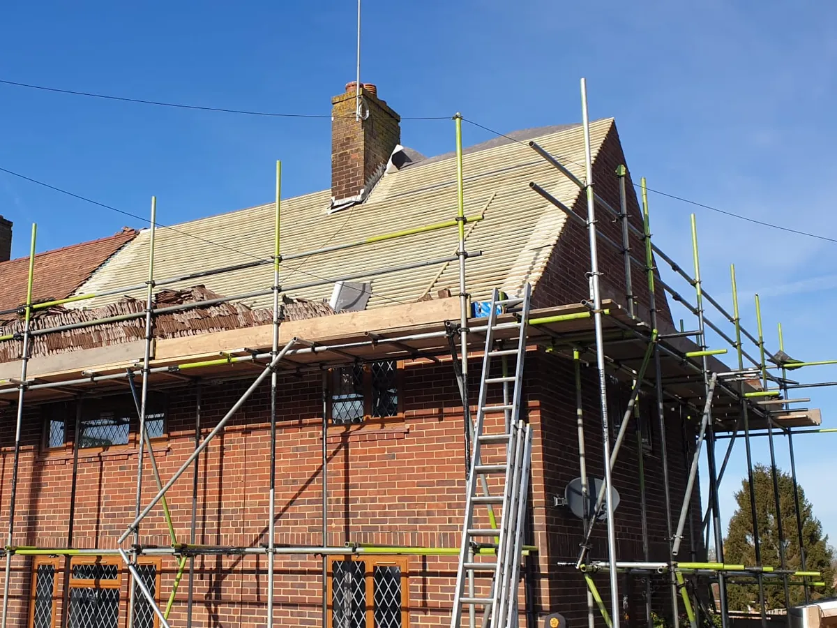 Brick chimney on a roof stripped to new battens, with scaffolding