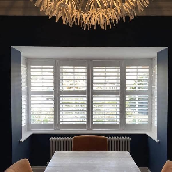 White shutters in a bay window of a navy dining room