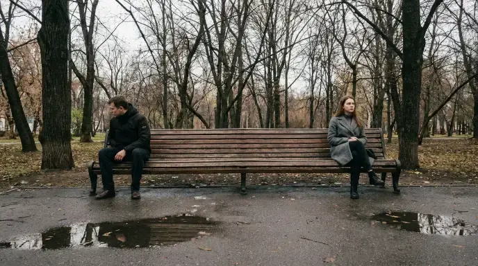 Two adults sitting apart on a park bench, symbolizing the trust issues and relationship difficulties that can develop in adulthood as a result of early childhood trauma.