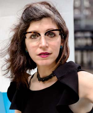 Image of Shellie Schmals in a black dress smiling wearing glasses with black necklace