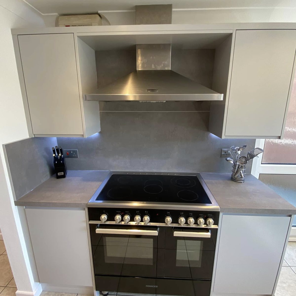 Range cooker between grey units with a stainless chimney hood, fitted in Suffolk by tradeMark Kitchens
