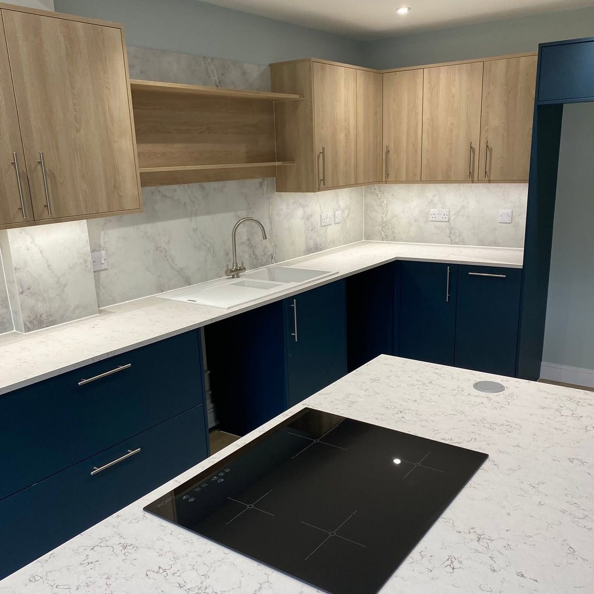 L-shaped navy and oak kitchen with marble effect splashback and quartz worktops, fitted by tradeMark Kitchens