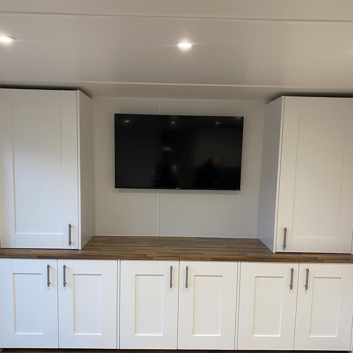 White shaker fitted cabinets and media wall with oak worktop