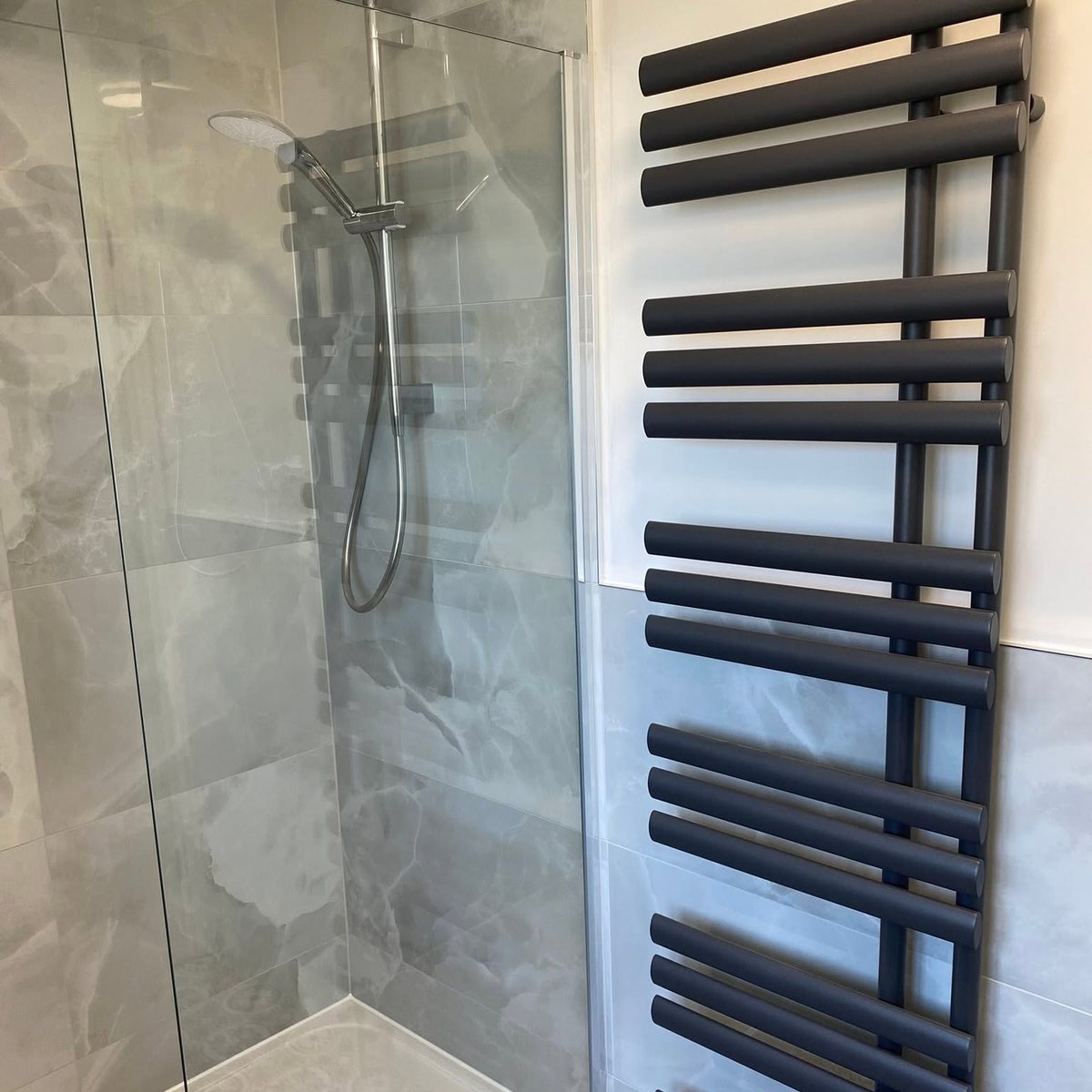 Walk-in shower with marble effect tiles and anthracite towel radiator