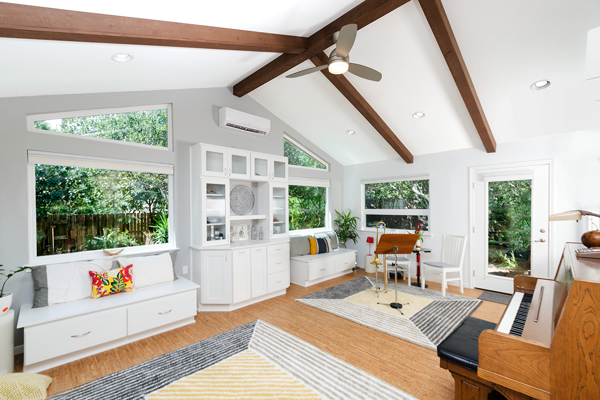 Bright remodeled living room with vaulted ceiling, exposed wood beams, large windows, built-in cabinetry, and natural light photographed for a remodeling contractor portfolio. Bright remodeled living room with vaulted ceiling, exposed wood beams, large windows, built-in cabinetry, and natural light photographed for a remodeling contractor portfolio.