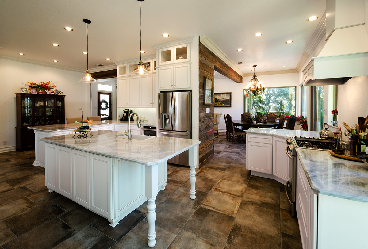 Remodeled kitchen with white cabinetry, large marble island, pendant lights, wood beam accents, and open dining area photographed for a contractor portfolio. Remodeled kitchen with white cabinetry, large marble island, pendant lights, wood beam accents, and open dining area photographed for a contractor portfolio.