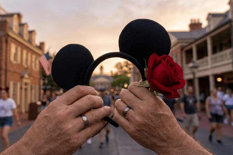 Dos manos con orejas Disney y una rosa, detalle romántico en el parque