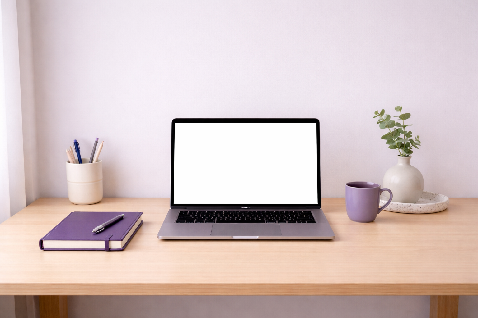 A minimal, uncluttered desk with a single notebook and laptop, in a clean white workspace with a soft lilac accent, suggesting calm and operational clarity.