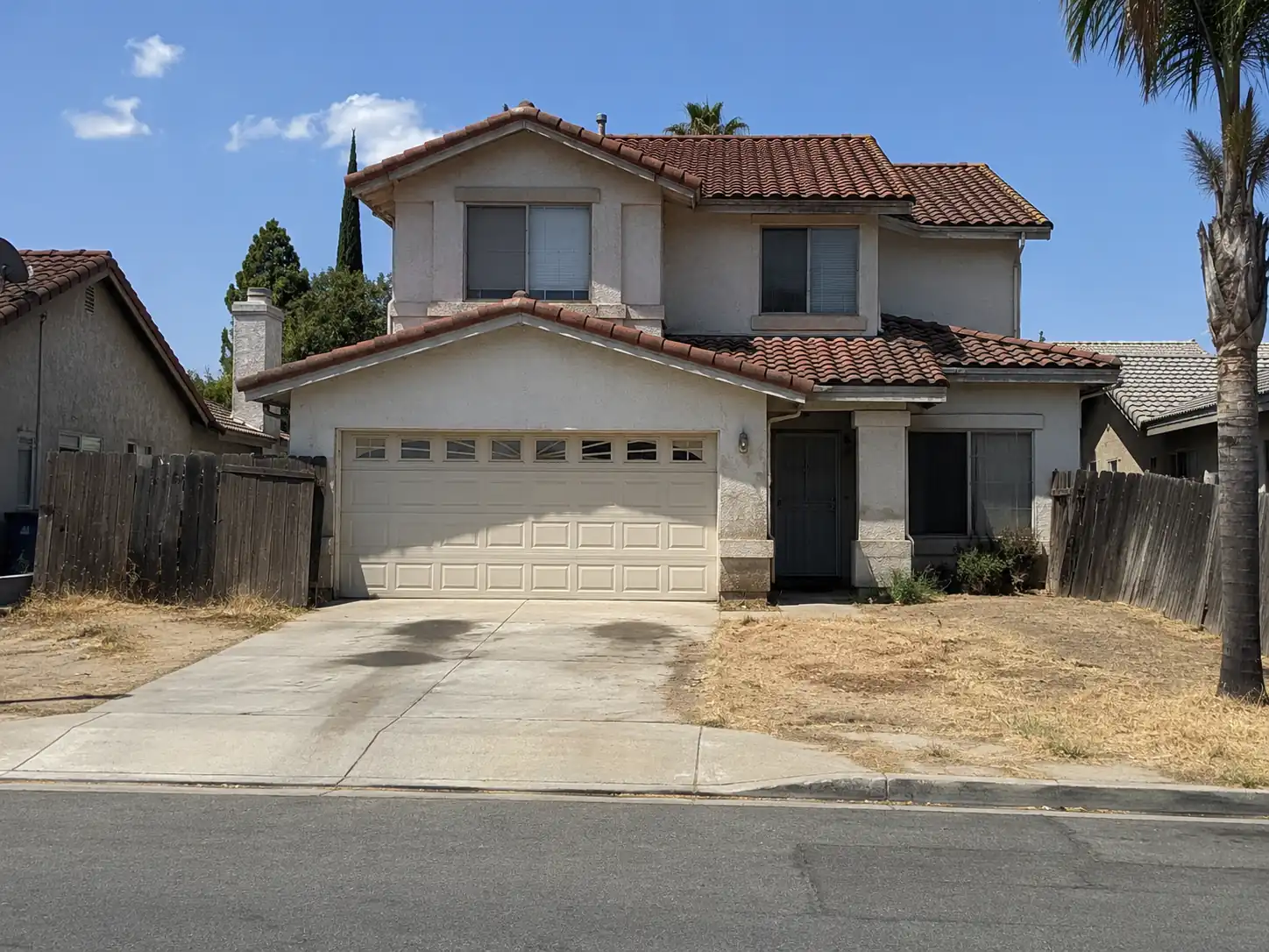 Two-story stucco house with a tile roof and dry front lawn in Fontana, CA