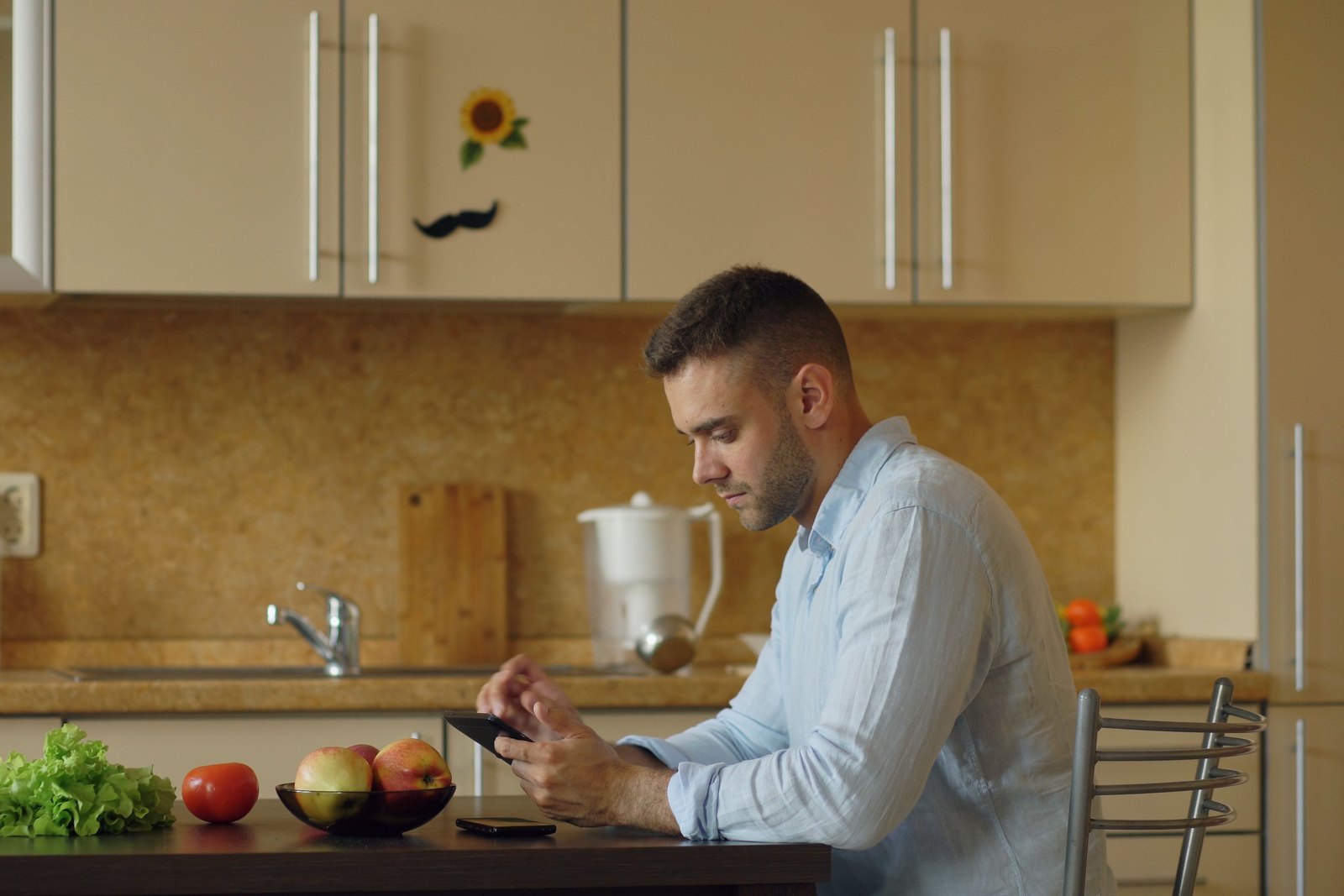 A man at his kitchen table looks at his phone.