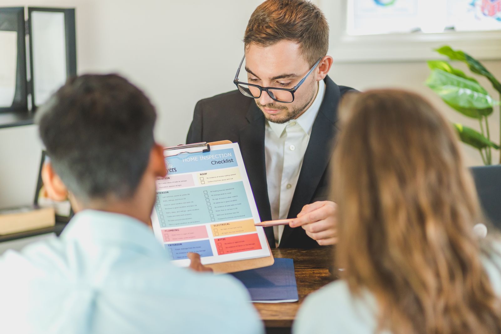 An agent walks two clients through a home inspection checklist at a desk.