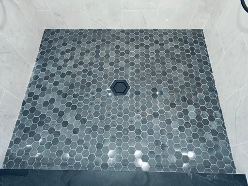 Charcoal hex-mosaic shower floor with a black hex drain, bordered by marble-look porcelain tile