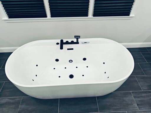Freestanding soaker tub with jet ports and a matte-black tub filler under a shuttered window