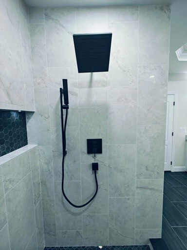 Matte-black square rain shower head, handheld on a slide bar, and wall valve on marble-look porcelain tile