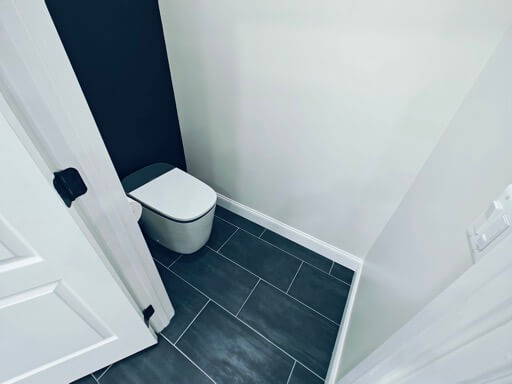 Private water closet with a navy accent wall, skirted toilet, and dark plank tile floor