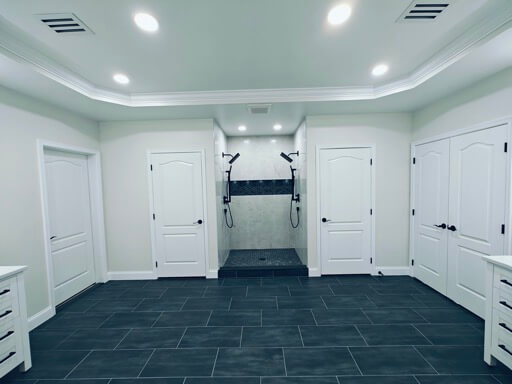 Wide view across the finished master bathroom, a white vanity on each wall with the walk-in shower centered between them