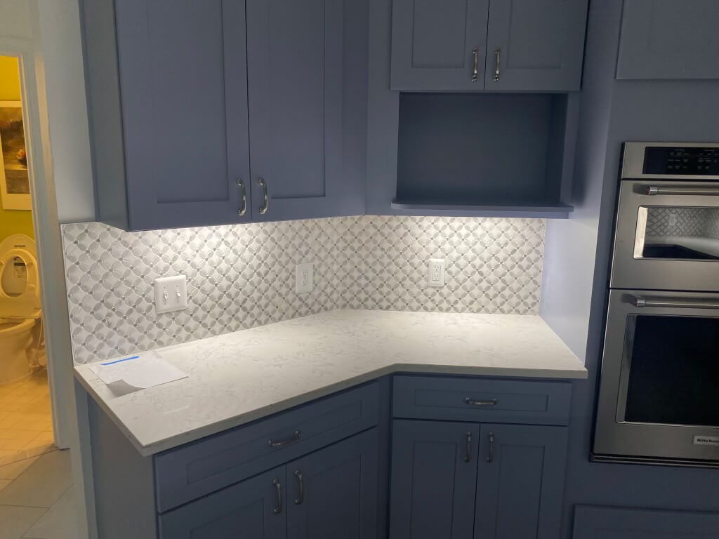 Finished kitchen corner with a built-in stainless double wall oven, slate blue-gray cabinets, and a marble arabesque mosaic backsplash