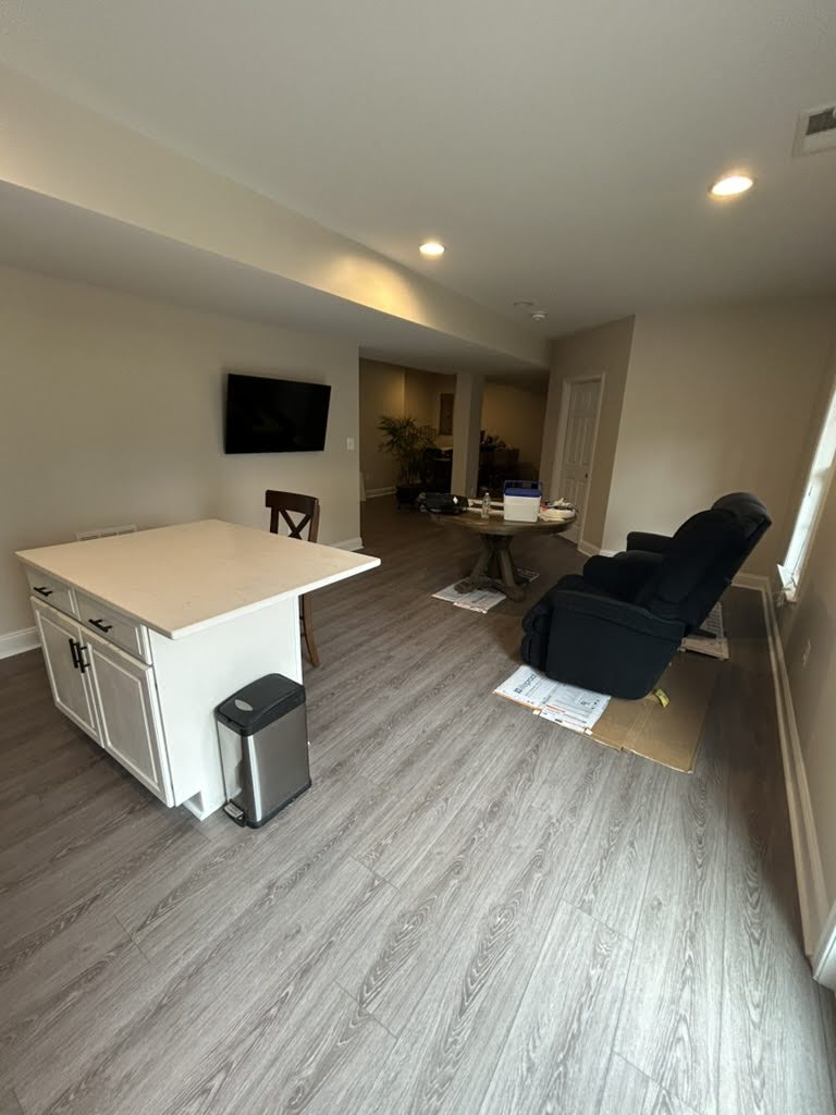 Finished basement living area in Dominion Valley, Haymarket VA, with gray water-resistant LVP flooring and a new white island with built-in outlets