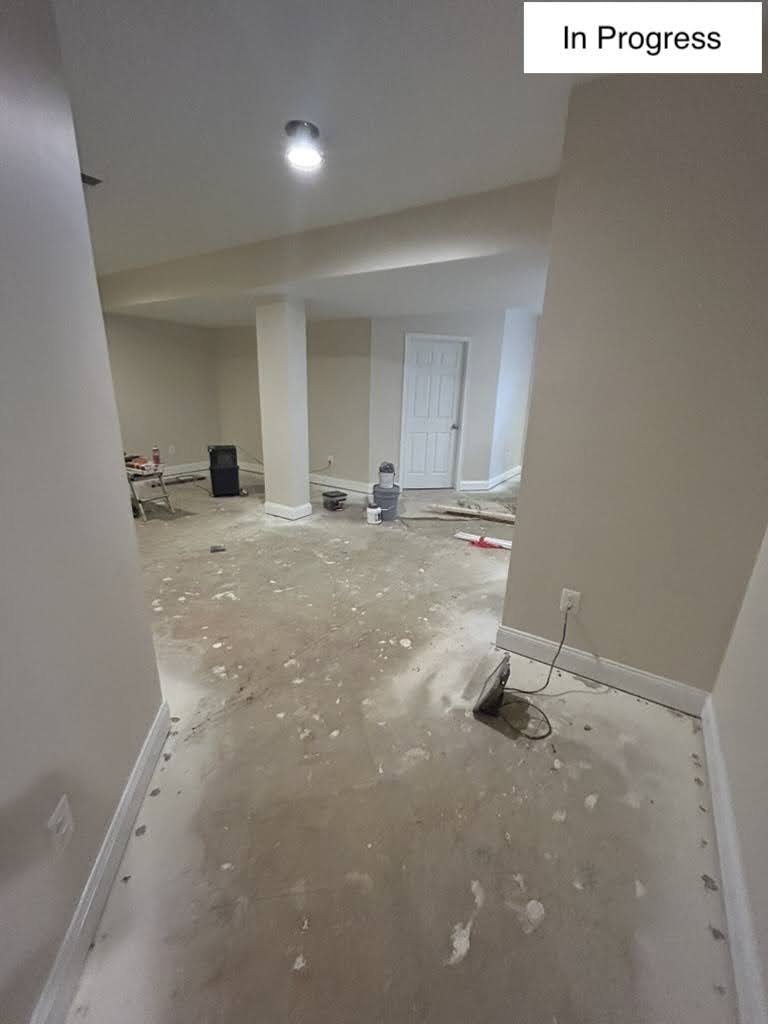 Unfinished basement before remodeling, with a bare concrete floor, a wrapped support column, and primed drywall
