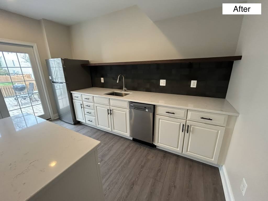 Finished basement wet bar with white shaker cabinets, quartz counter, dark tile backsplash, stainless refrigerator and dishwasher, and a walk-out to the patio