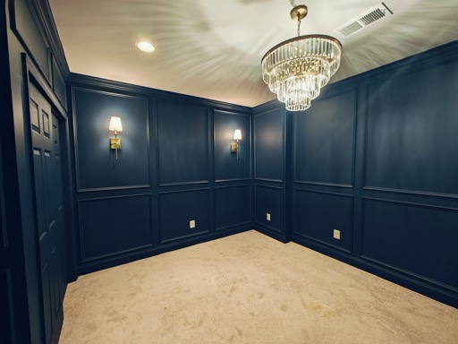 Basement bedroom corner with full-height navy picture-frame millwork and brass wall sconces